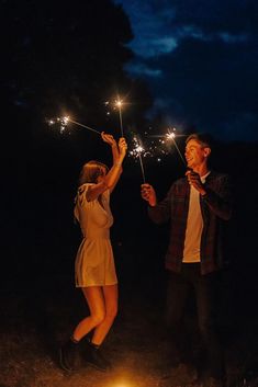 a man and woman holding sparklers in their hands while standing next to a campfire