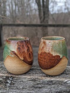 two cups sitting on top of a wooden table next to each other in front of some trees