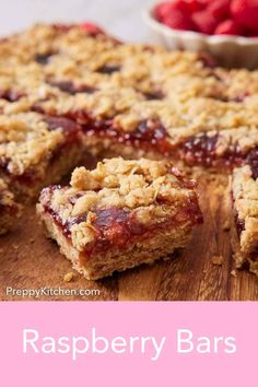 raspberry bars cut into squares on top of a cutting board with strawberries in the background