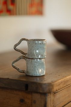 two coffee mugs sitting on top of a wooden table in front of a bowl