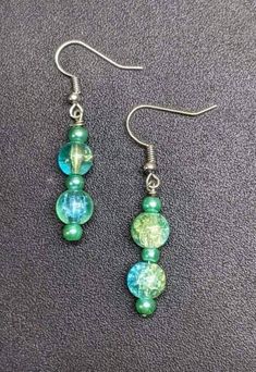 green and blue glass beaded earrings with silver earwires on a gray surface