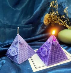 two pyramid shaped candles sitting on top of a blue cloth next to a vase with flowers