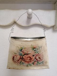 an old tin can with flowers painted on it hanging from a white hook in a room