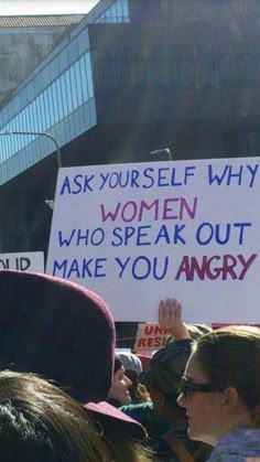 a group of people holding up signs in front of a building that says ask yourself why women who speak out make you angry