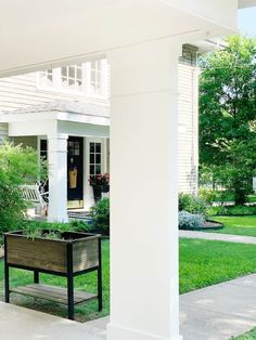 a wooden planter sitting on the side of a white house next to a bench