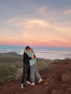 a man and woman hugging on top of a mountain with the sky in the background