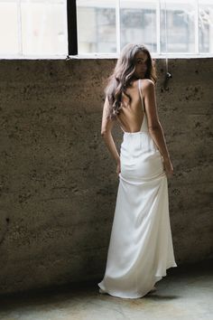 a woman standing in front of a window wearing a white dress and looking down at the floor