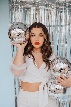 a woman holding two disco balls in front of her face and posing for the camera