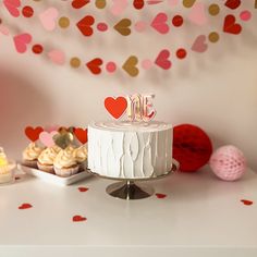 a white cake sitting on top of a table next to cupcakes