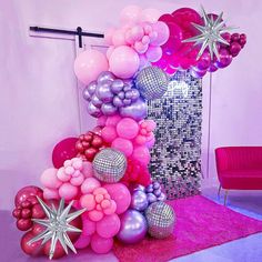 a bunch of balloons that are on the ground in front of a pink chair and wall