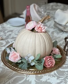 a white pumpkin decorated with pink flowers on a gold platter sitting on a table