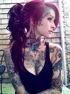 a woman with tattoos on her neck and chest standing in front of a brick wall