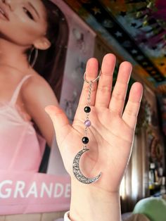 a person holding their hand up to the sky with a crescent moon charm hanging from it