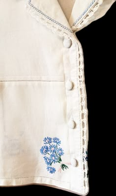 a white shirt with blue flowers on the front and back buttons down the chest, along with lace trimmings