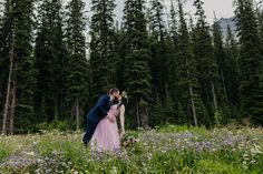 a bride and groom kissing in a field of wildflowers with trees in the background