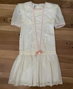 "Lovely vintage Gunne Sax by Jessica McClintock dress Girls Size 8 Appears new and unworn with some discoloration on inside of dress at shoulder pads from hanger Semi-sheer lightweight fabric with woven muslin appearance. Fully lined bodice and skirt. Drop waist with lace trim and hem Oversized large lace collar with a peachy pink ribbon detail on bodice Chest measures 15\" across, armpit to armpit Waist: 15\" across Total length: 34\" from shoulder to bottom of lace hem" Cream Lined Dresses For Daywear, Retro Short Sleeve Dresses With Lace Trim, Off White Lace Trim Dress For Daywear, White Vintage Dress With Short Sleeves And Lining, Feminine Vintage Cream Dress With Lace Trim, Vintage White Dress With Yoke, Vintage White Dress With Yoke Detail, White Lined Vintage Dress For Daywear, Feminine White Vintage Dress For Daywear