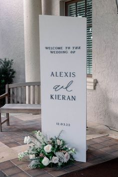 a welcome sign with flowers and greenery in front of a building that says, welcome to the wedding of alexis and kieran