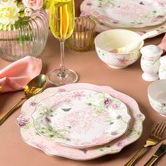 the table is set with pink and green china plates, silverware, and champagne glasses