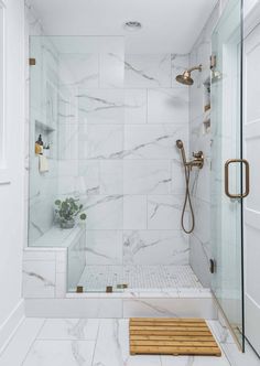 a walk in shower sitting next to a white tiled wall and wooden bench on the floor