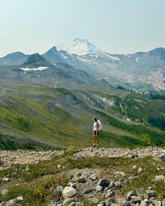 a person standing on top of a rocky hill with mountains in the background and snow capped peaks