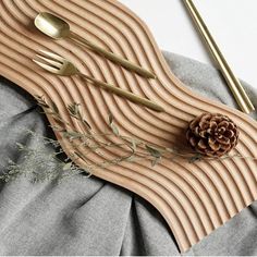 a wooden cutting board with forks and spoons on it next to a pine cone