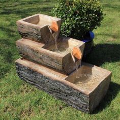 a wooden fountain in the grass next to a potted plant and tree stumps