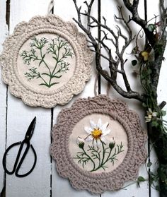 three handmade wall hangings with flowers on them next to scissors and twig