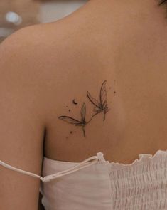 the back of a woman's shoulder with a small dragonfly tattoo on it