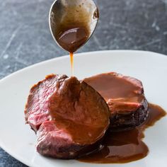 a spoon drizzling sauce onto some meat on a white plate with brown gravy