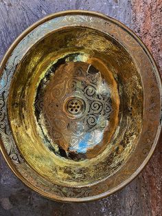 an ornate gold bowl is sitting on a stone surface with a circular design in the center