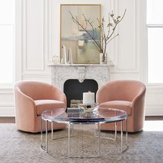 a living room with two pink chairs and a coffee table in front of a fireplace