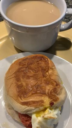 a breakfast sandwich on a plate next to a cup of coffee