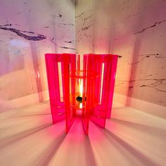 a bright pink lamp sitting on top of a white table next to a marble wall