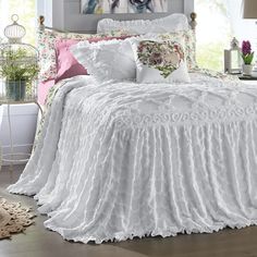 a white bed with ruffled bedspread and pillows