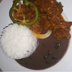 a white plate topped with rice and meat covered in gravy next to green peppers