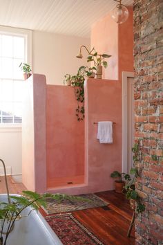 a bathroom with pink walls and wooden flooring next to a bathtub filled with plants