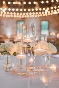 the centerpieces are filled with white flowers, candles and votive glass vases