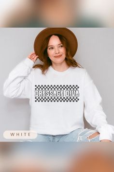 Woman dressed in a white sweatshirt that reads "Dressage Diva" in bold text with a checkered pattern behind it. She adds a stylish touch with a wide-brimmed brown hat and ripped jeans, giving the image a casual, fashionable vibe. Dressage Clothes, Equestrian Life, Girl Shirt, Horse Girl, The Horse, Horse Lover, Dressage