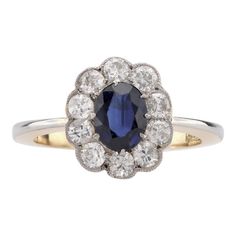 Center Stone: Oval Cut Blue Sapphire  Weight: Approximately .90 Carat Accent Stone: 10 Transitional Cut Diamonds Weight: Approximately .80 Carats Color: H Clarity: SI-I Metal: 18K Yellow Gold and Platinum  Era: Modern  Circa: 2020's in The Style of Edwardian  Hallmarks: Purity Marks Size: 7.5 and can be resized Gram weight: 4.61   This exquisite Edwardian-inspired cluster ring, crafted in a blend of 18K yellow gold and platinum, showcases a stunning .90 carat oval cut blue sapphire at its center. Surrounding the sapphire are 10 transitional cut diamonds, totaling approximately .80 carats, with H color and SI-I clarity, adding a touch of vintage charm to the modern design. Weighing 4.61 grams and sized at 7.5, this elegant piece from the 2020s combines the timeless beauty of Edwardian style Vintage Cocktail Ring, Edwardian Style, Edwardian Fashion, European Cut Diamonds, Sapphire Stone, Sapphire Diamond, Ring Size 7, Cluster Ring, Cocktail Rings