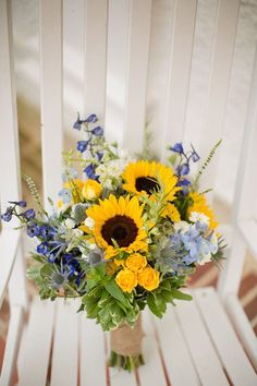 a bouquet of sunflowers and blue flowers on a white chair with wood slats