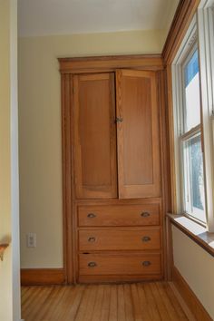 an empty room with wooden floors and cabinets in the corner, next to a window