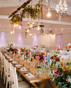 a long wooden table topped with lots of tables covered in white clothed chairs next to tall vases filled with flowers and candles