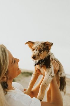 a woman holding a small dog in her arms on the beach while looking at the sky