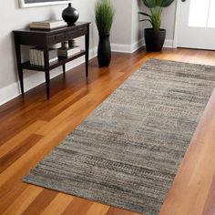 a living room with wooden floors and white walls, two planters on either side of the area rug