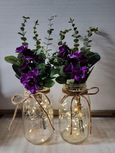 two mason jar vases with purple flowers and fairy lights on the lids are sitting on a table