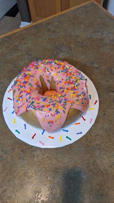 a pink frosted doughnut with sprinkles on a white platter