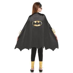 a girl in a batman cape and leggings is standing with her back to the camera