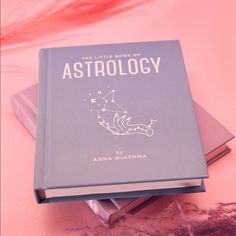 the little book of astrology sits on top of each other next to some feathers