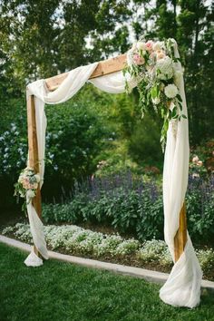 an outdoor wedding ceremony with white draping and flowers on the arch, surrounded by greenery