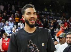 a man standing in front of a crowd wearing a black shirt with a basketball on it